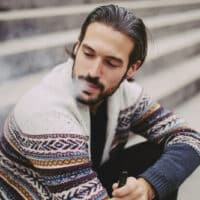 Junger Mann sitzt auf einer Treppe im Freien und raucht eine E-Zigarette