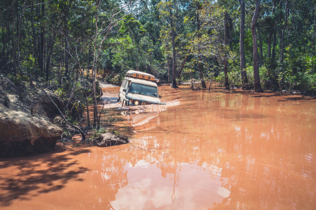 Jeep fährt durch braunen Fluss im Wald.