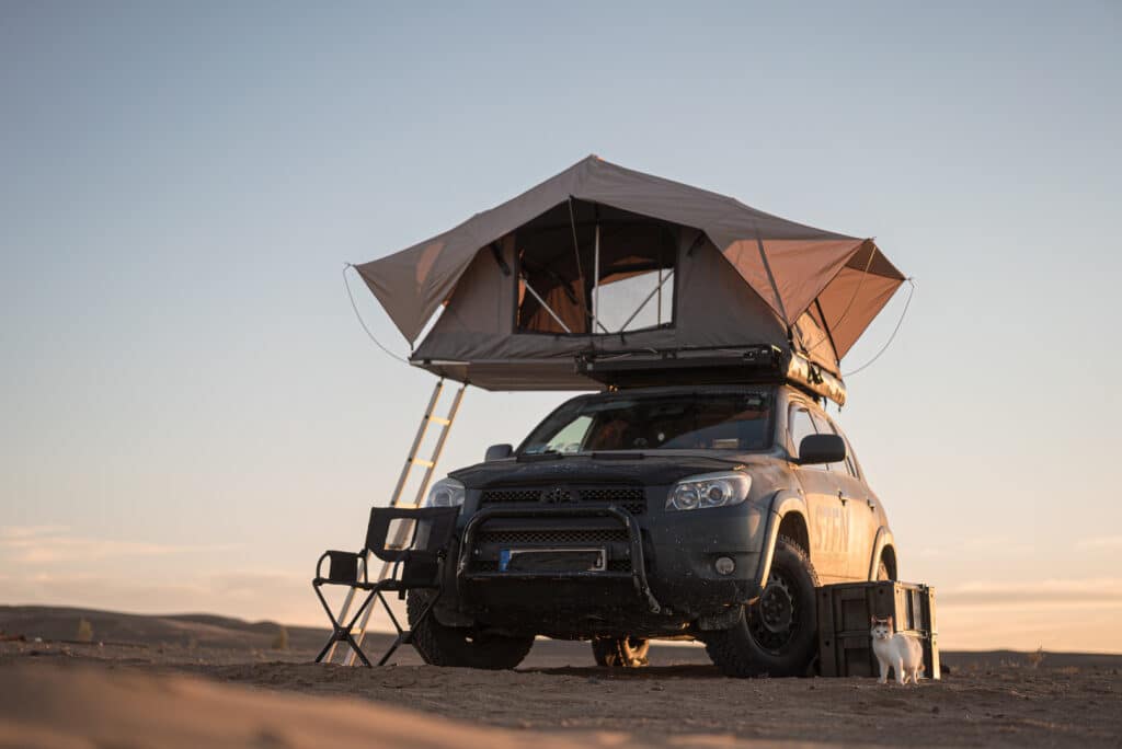 A rooftop tent for camping on the roof rack of an off-road SUV car in a desert