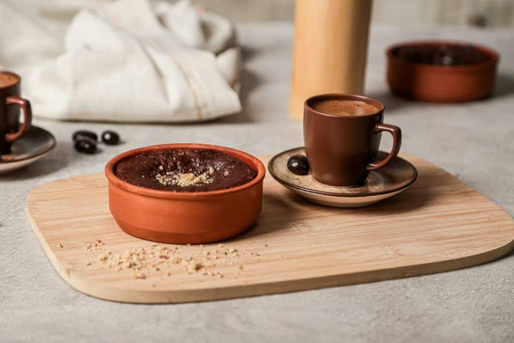 Tasse Kaffee mit Schokobohne und Keramikschale mit warmem Schokokuchen auf einem Holztablett