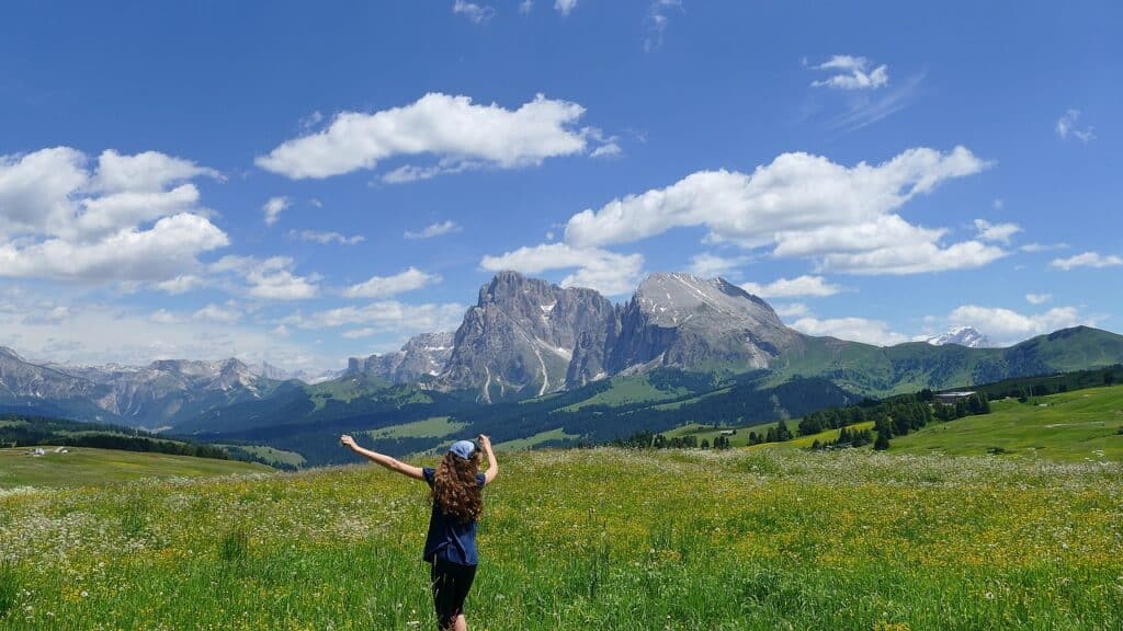 Junge Frau läuft beschwingt durch die Wiesen der Seiser Alm im Sommer im Hintergrund die Dolomiten