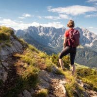 Wanderin mit rotem Rucksack auf Bergpfad mit Blick auf Bergmassiv