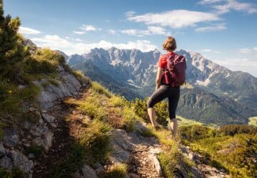 Wanderin mit rotem Rucksack auf Bergpfad mit Blick auf Bergmassiv