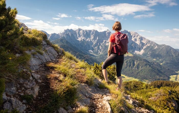 Wanderin mit rotem Rucksack auf Bergpfad mit Blick auf Bergmassiv