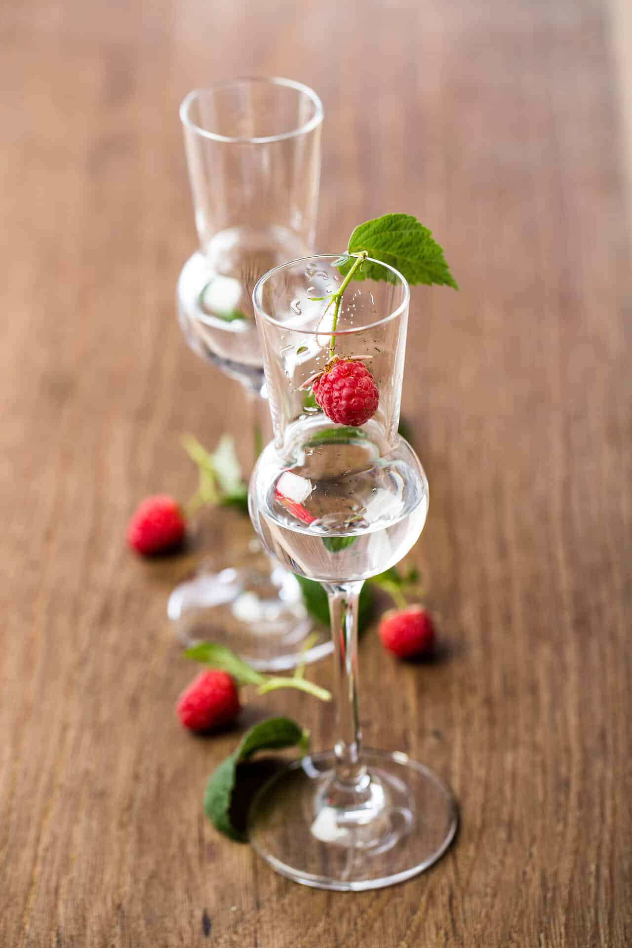 2 Gläser Himberschnaps auf einem Holztisch dekoriert mit kleinen Waldhimbeeren