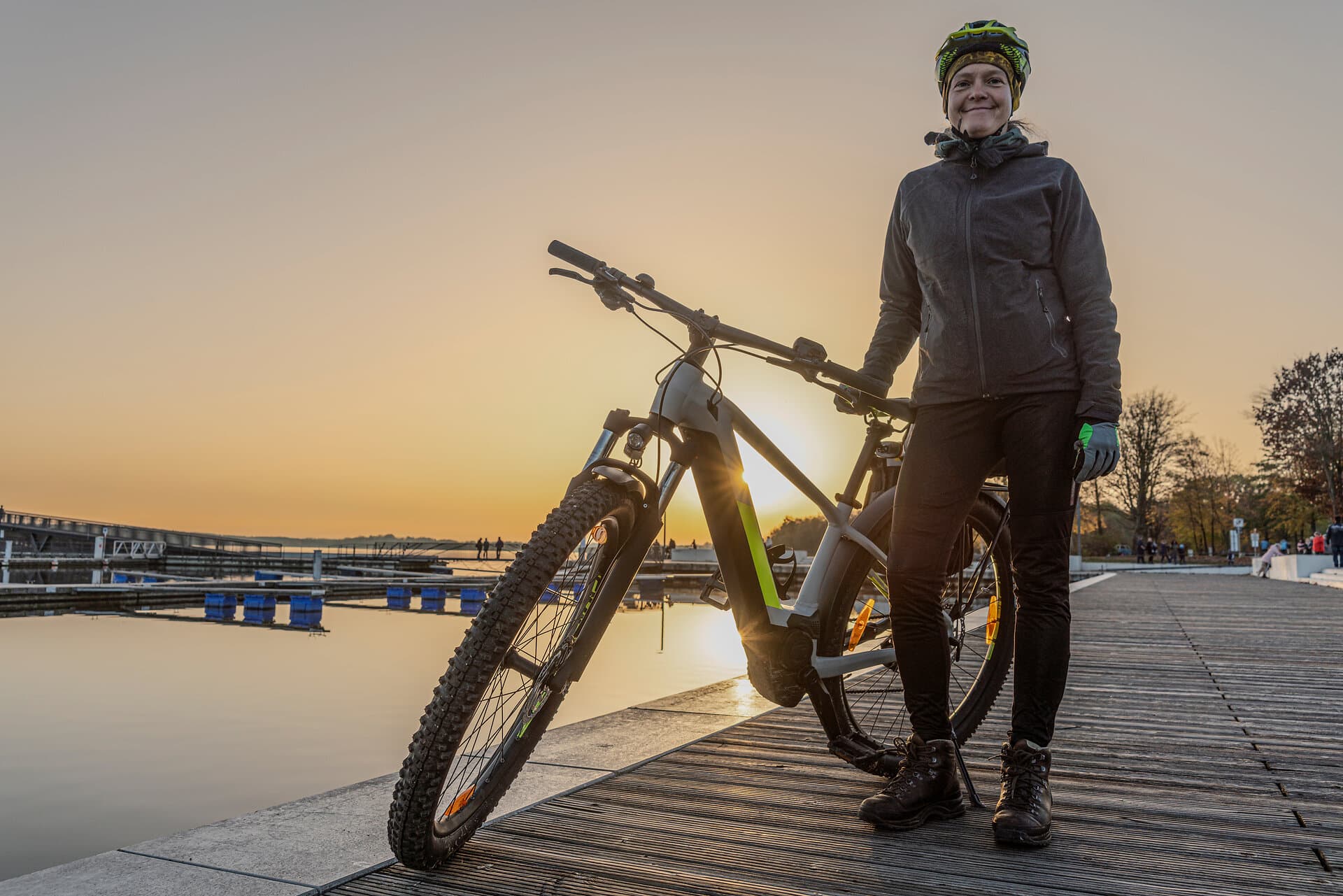 Junge Frau in Radkleidung im Winter mit Fahrrad auf einem Steg am See