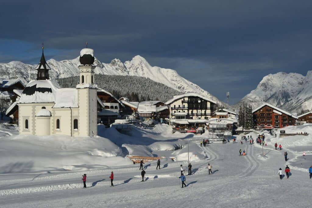 Verschneiter Ortskern von Seeefeld in Tirol mit Seekirchl bei Sonnenschein mit Spaziergängern und Skilangläufern