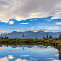 Wanderer springt durch die Luft am Seeufer bei Seefeld in Tirol vor Bergkulisse