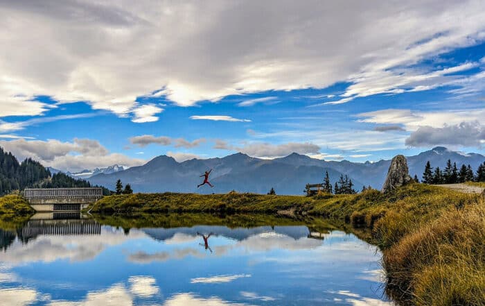 Wanderer springt durch die Luft am Seeufer bei Seefeld in Tirol vor Bergkulisse