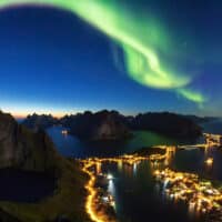 Grünes Polarlicht über Abendhimmel auf den Lofoten in Norwegen mit den Lichtern der Stadt aus der Luft fotografiert