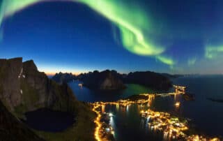 Grünes Polarlicht über Abendhimmel auf den Lofoten in Norwegen mit den Lichtern der Stadt aus der Luft fotografiert