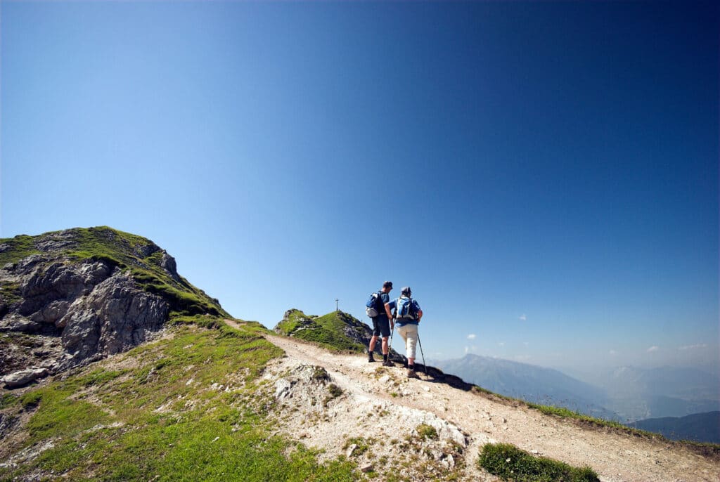 2 Wanderer aufs Gebirgsweg im Sommer bei blauem Himmel mit Panoramaausblick.