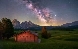 Blick auf eine Hütte auf der Seiser Alm am Abend mit Sternenhimmel und Milchstraße - Astrotourismus