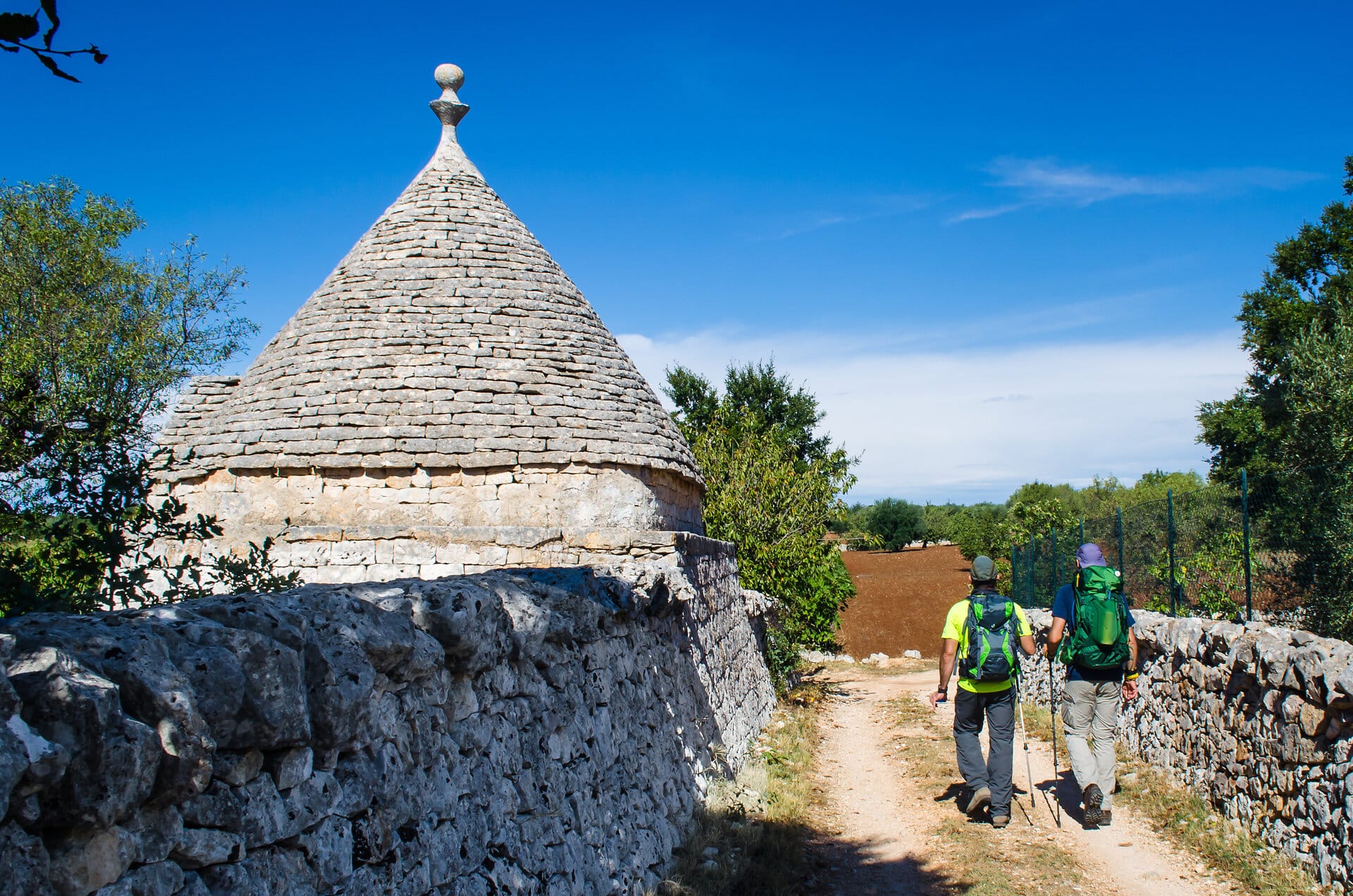 2 Wanderer im Sonnenschein passieren einTrulli in Italien