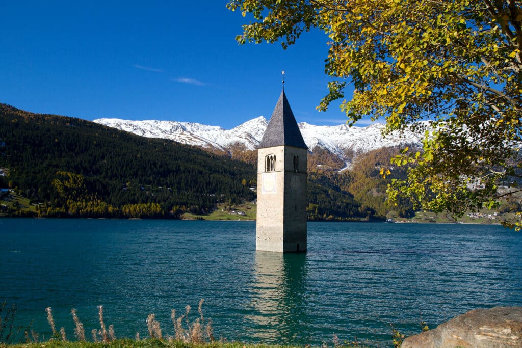 Reschensee mit versunkenem Kirchturm und schneebedeckten Bergen im Hintergrund