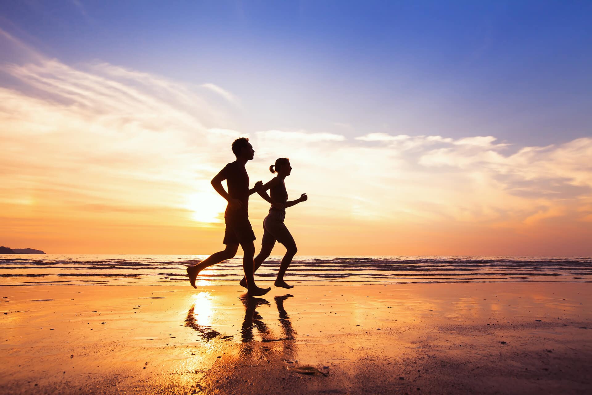 Pärchen joggt barfuß am Strand im Sonnenuntergang