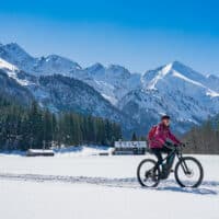 Frau fährt mit dem Fahrrad durch Allgäuer Schneelandschaft