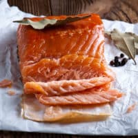 Geräucherter Lachs auf weißem Papier mit Lorbeerblatt und Wacholderbeeren