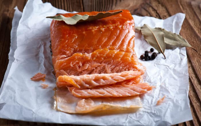 Geräucherter Lachs auf weißem Papier mit Lorbeerblatt und Wacholderbeeren