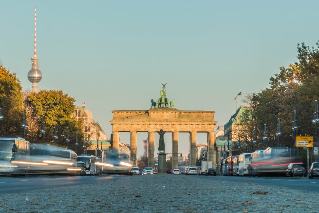 Bewegter Verkehr vor dem Brandenburger Tor in Berlin bei blauem Himmel im Spätsommer im Hintergrund ist der Berliner Fernsehturm sichtbar