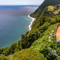 Wunderschöner Küstenwanderweg auf den Azoren an einem sonnigen Tag mit blühenden Hortensien und tiefblauem Meer