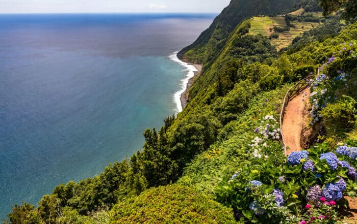 Wunderschöner Küstenwanderweg auf den Azoren an einem sonnigen Tag mit blühenden Hortensien und tiefblauem Meer