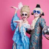 Energetic couple in baroque costumes poses joyfully against a vibrant pink background, capturing the essence of a themed carnival