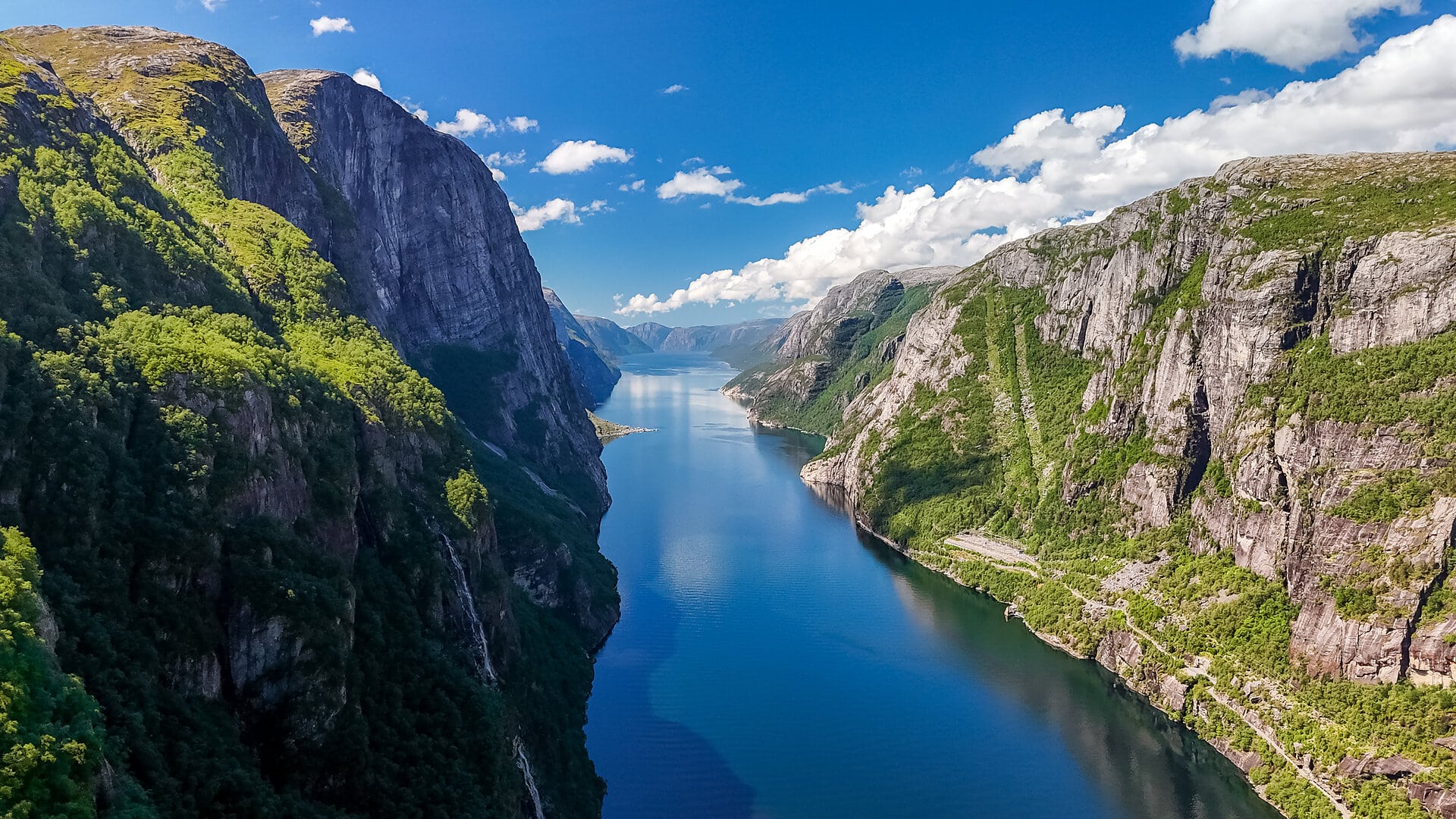 A breathtaking view of a Norwegian fjord, showcasing towering cliffs, lush greenery, and the crystal-clear waters of the fjord. Kjerag, Lysebotn, Lysefjorden, Norway