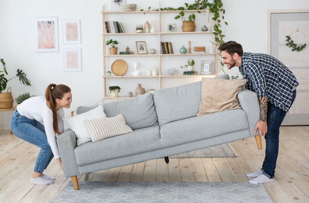 Junges paar stellt graues Sofa in der Wohnung auf.