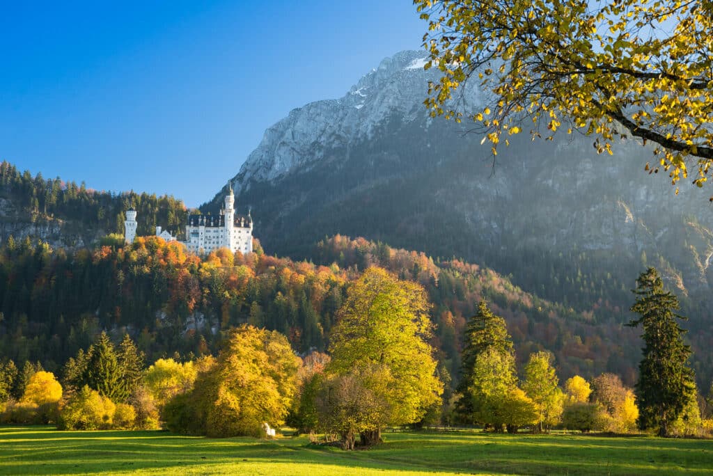 Blick auf Schloss Neuschwanstein und das Ammergebirge im Herbst bei Sonnenschein