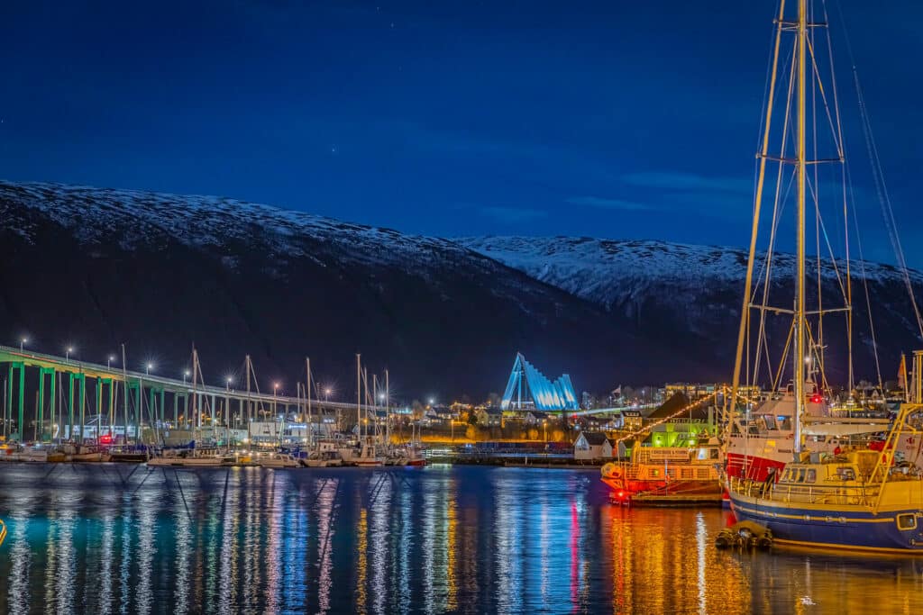 Hafen in Tromso am Abend mit beleuchteten Boote und der hell erleuchteten Eismeerkathedrale